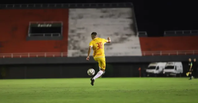 Soccer player in yellow jersey kicking a ball on a green pitch during night match under lights.