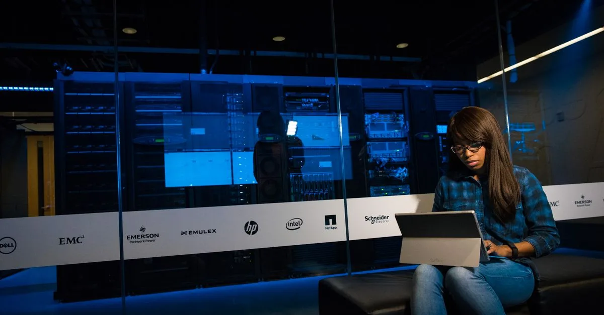 Woman using a laptop in a server room, showcasing modern technology and work environment.