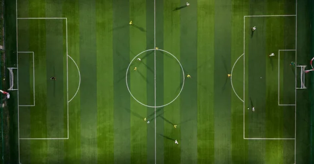 Dynamic aerial shot capturing a soccer match on a vibrant green field at night.