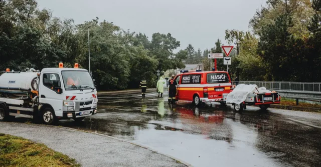 Emergency services attending a scene on a rainy road with rescue vehicles and personnel.