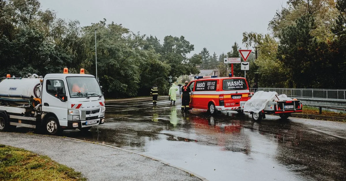 Emergency services attending a scene on a rainy road with rescue vehicles and personnel.
