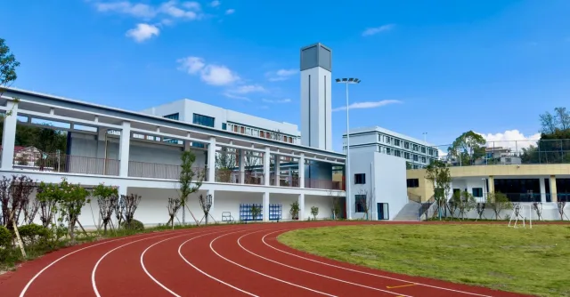A modern sports facility with a red running track and towers on a sunny day.