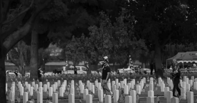 Black and white scene of people visiting a war memorial, displaying tributes and remembrance.