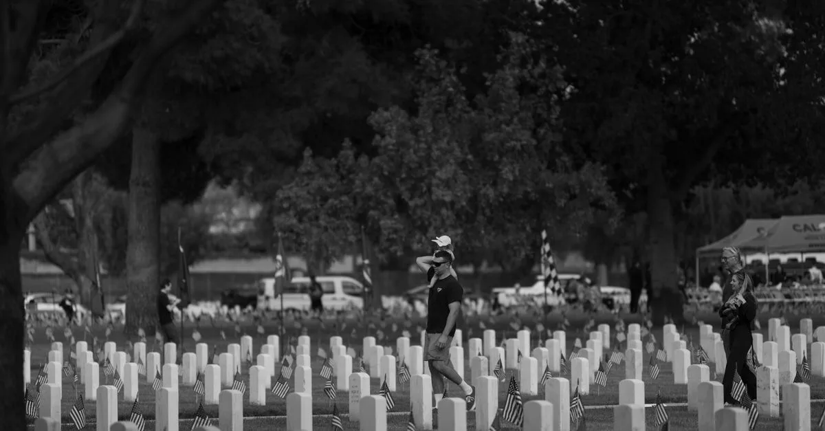 Black and white scene of people visiting a war memorial, displaying tributes and remembrance.