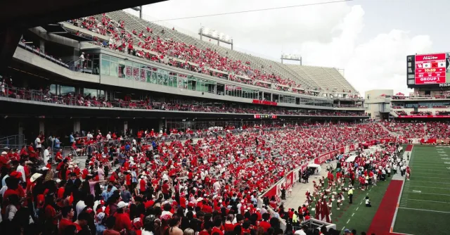 A vibrant crowd in a stadium cheering during an outdoor football game, creating an energetic atmosphere.