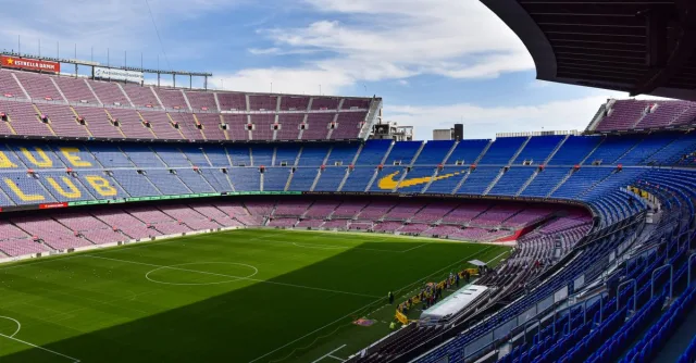 Wide view of the iconic Camp Nou stadium in Barcelona, showcasing its vast empty stands and lush green field.
