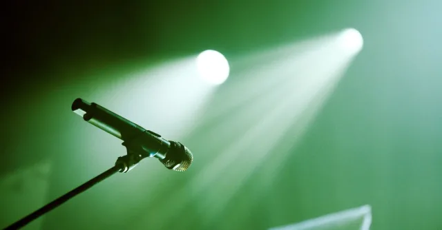 From below of black stand with microphone placed on stage with green illumination