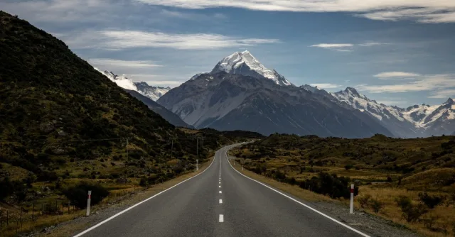 Smooth asphalt road going along green hills towards rocky valley with snowy peaks