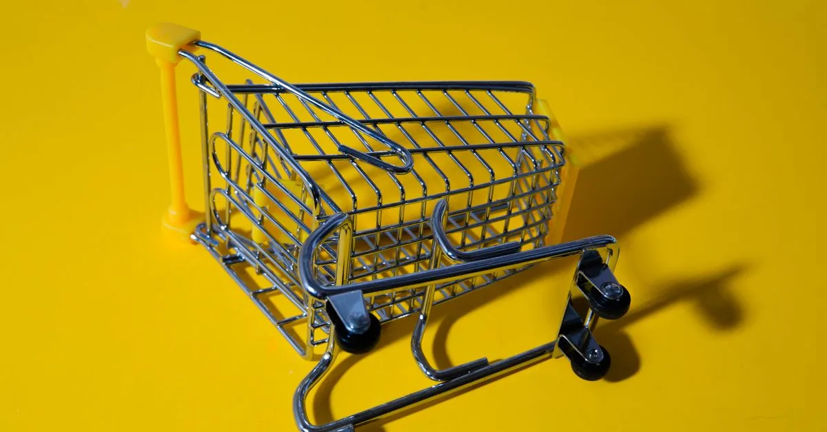 Close-up of a toy shopping cart on a vivid yellow surface, casting shadows.