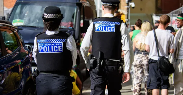 Metropolitan Police officers supervising a public gathering during daytime in an urban setting.