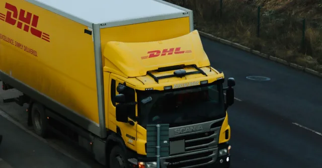 Yellow DHL delivery truck driving along a city road showcasing logistics in action.