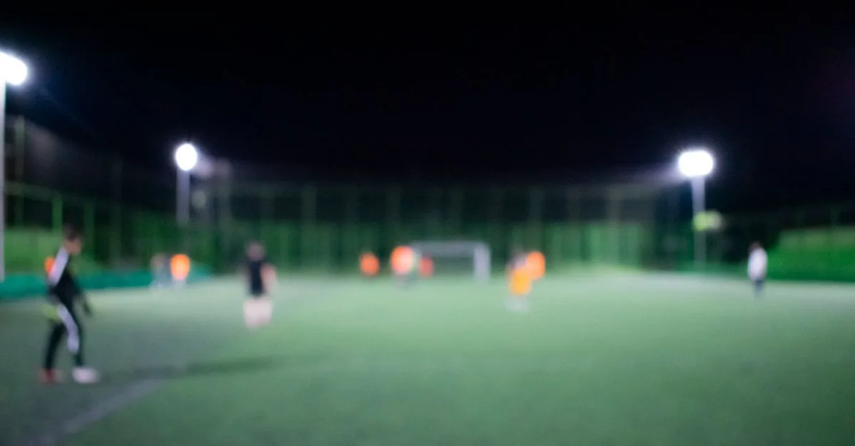 Blurred image of a nighttime football match under bright stadium lights with players on the field.