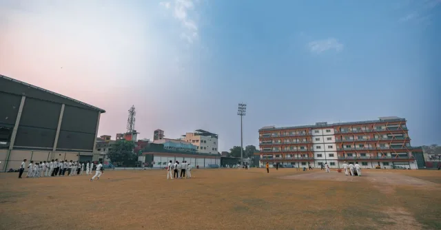 Outdoor cricket match on a sports field with players under a clear sky in Delhi, India.