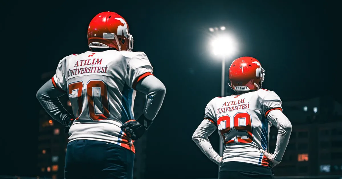 Football players in Atılım University jerseys standing under stadium lights at night.