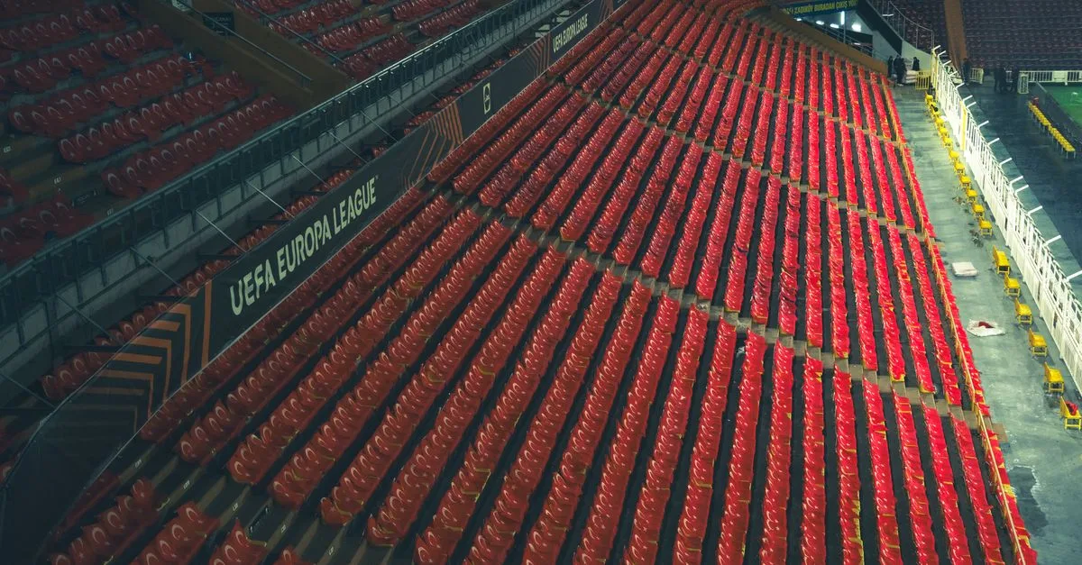 Rows of empty red seats in a UEFA Europa League stadium, captured from above.