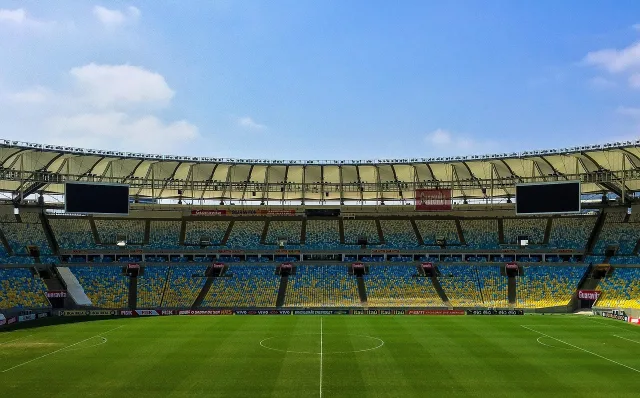 An illuminated football stadium under evening floodlights before a Premier League match.