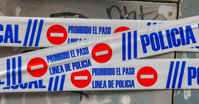 Police tape with 'Prohibido El Paso' against graffiti-covered wall. Crime scene concept.