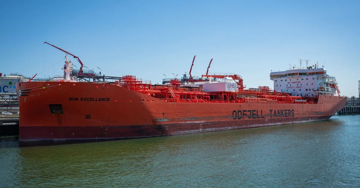 A large red oil tanker named Bow Excellence docked at a harbor under clear blue skies.