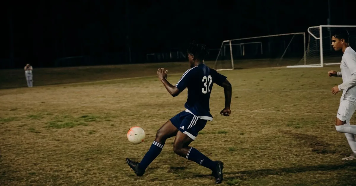 Two players compete fiercely during a nighttime football match on a grass field.