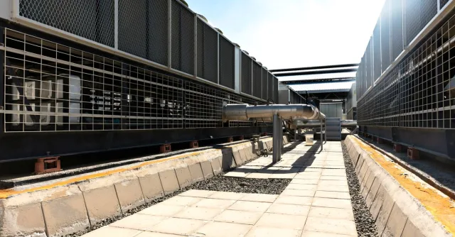 View of a large industrial cooling system with metal pipes and grids outdoors under bright daylight.