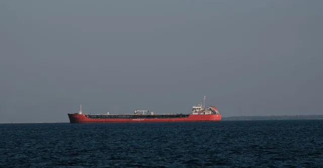 A red cargo ship sailing on the calm waters of İzmir Bay under a clear sky.