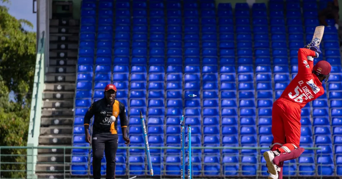 A cricket player in red batting during a match in an empty stadium with blue seats.