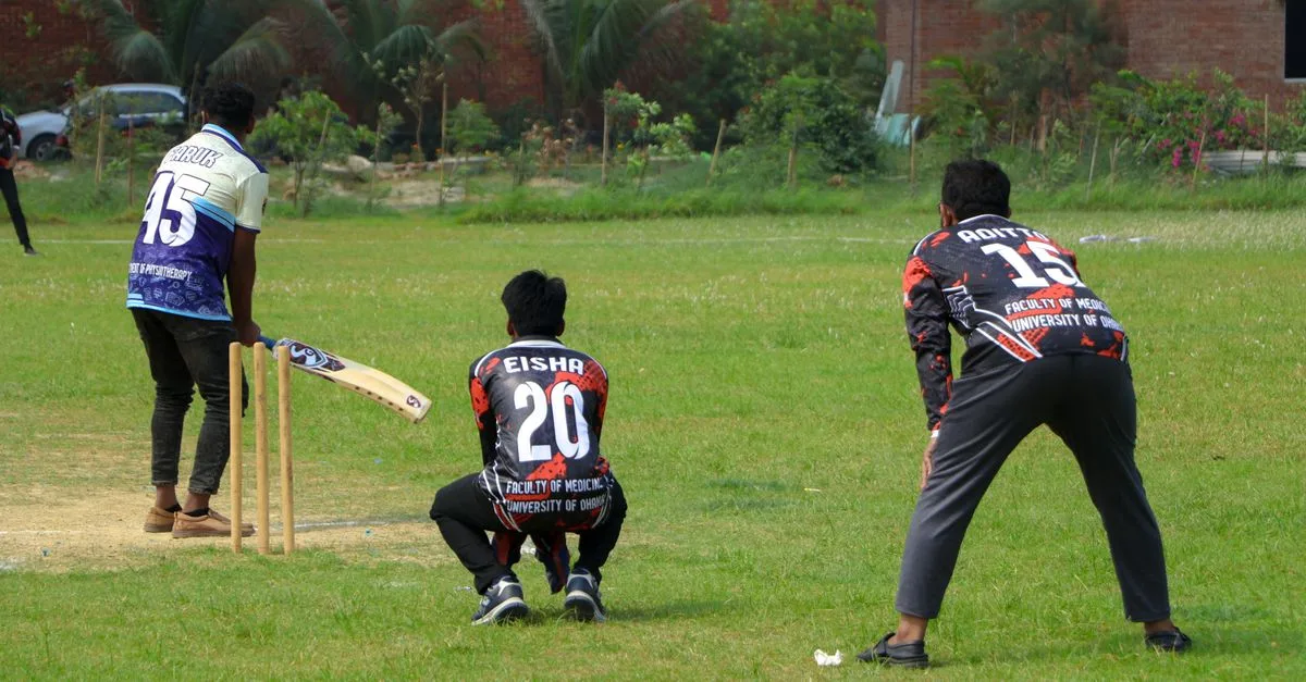 Cricket players in action on a sunny day at an outdoor field.