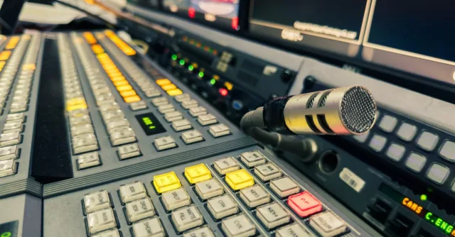 Detailed view of a broadcasting studio control panel with a microphone and multiple screens.
