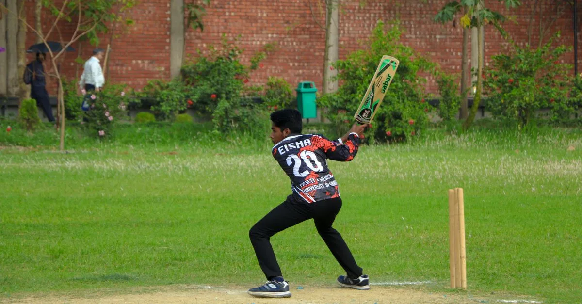 A young male cricketer takes a swing at the ball during a cricket match on a sunny day.