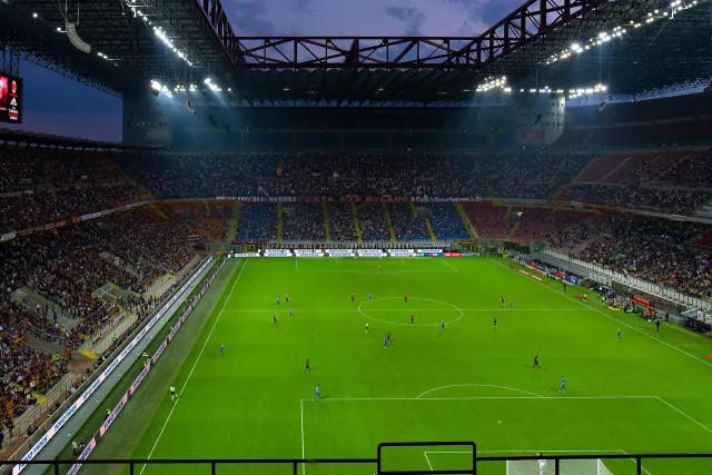 A football stadium illuminated under floodlights during an evening match.