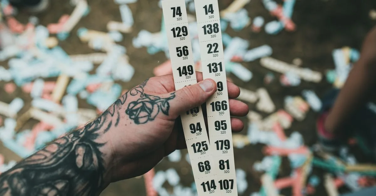 Close-up of a tattooed hand holding raffle tickets amidst confetti at a festival setting.