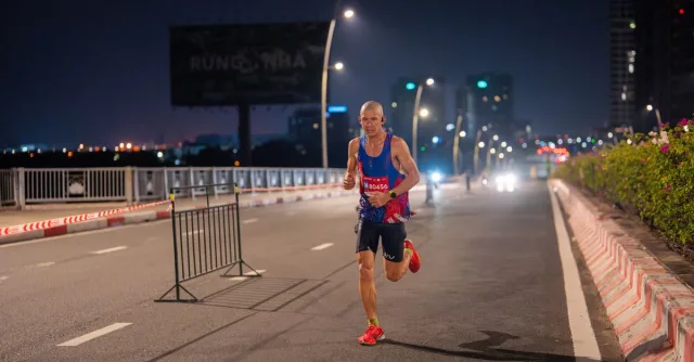 A focused runner competes in an urban marathon at night, road illuminated by streetlights.