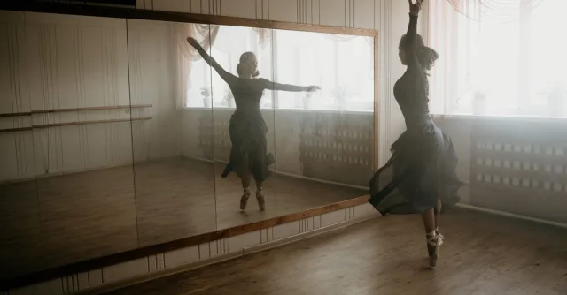 A graceful ballerina dances on pointe in a sunlit studio, capturing movement and reflection.