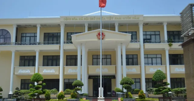 Front view of a government building in Phu Quoc, Vietnam, with a red flag and decorative plants.