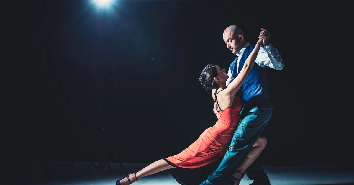 Elegant couple performing tango under a dramatic spotlight, showcasing passion and grace.