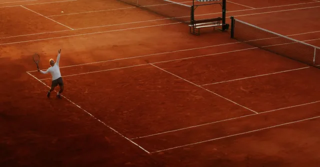 A player serves on a clay tennis court, highlighting the beauty and intensity of the sport at sunset.