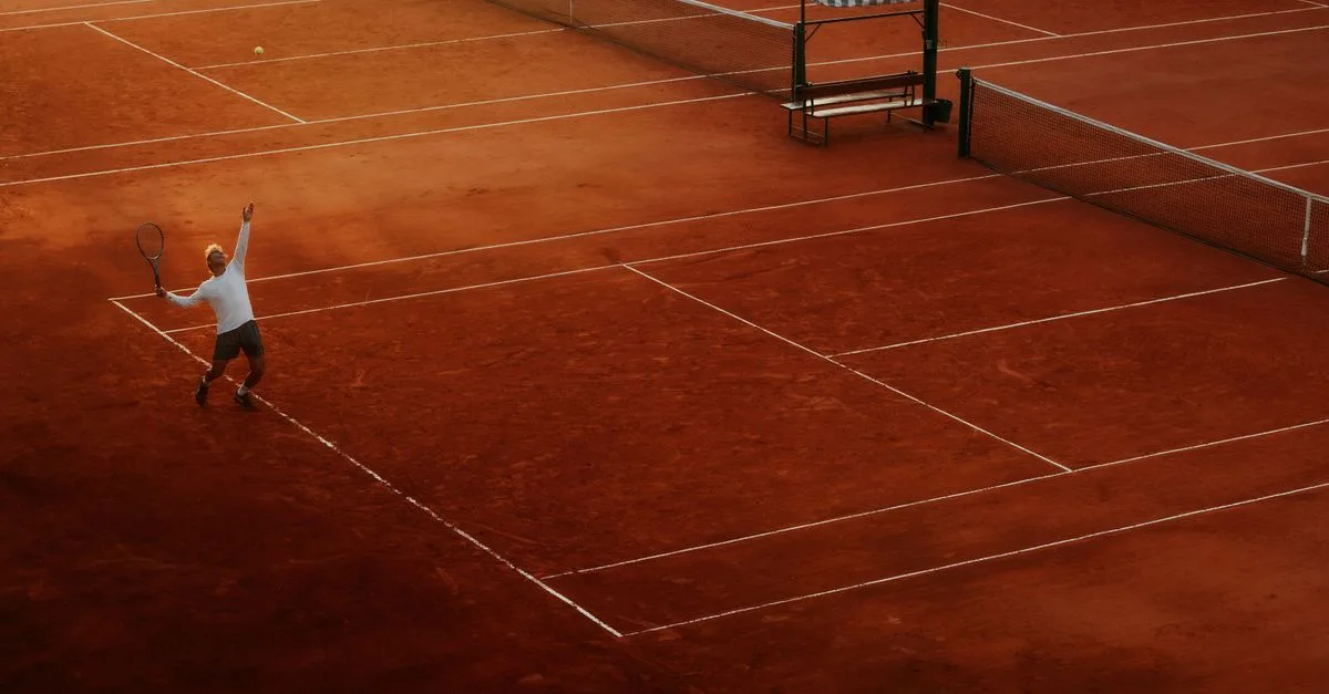 A player serves on a clay tennis court, highlighting the beauty and intensity of the sport at sunset.