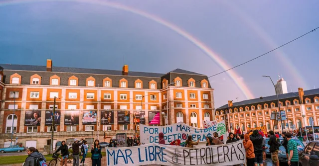 People protesting against oil exploration in Mar del Plata, Argentina under a striking double rainbow.