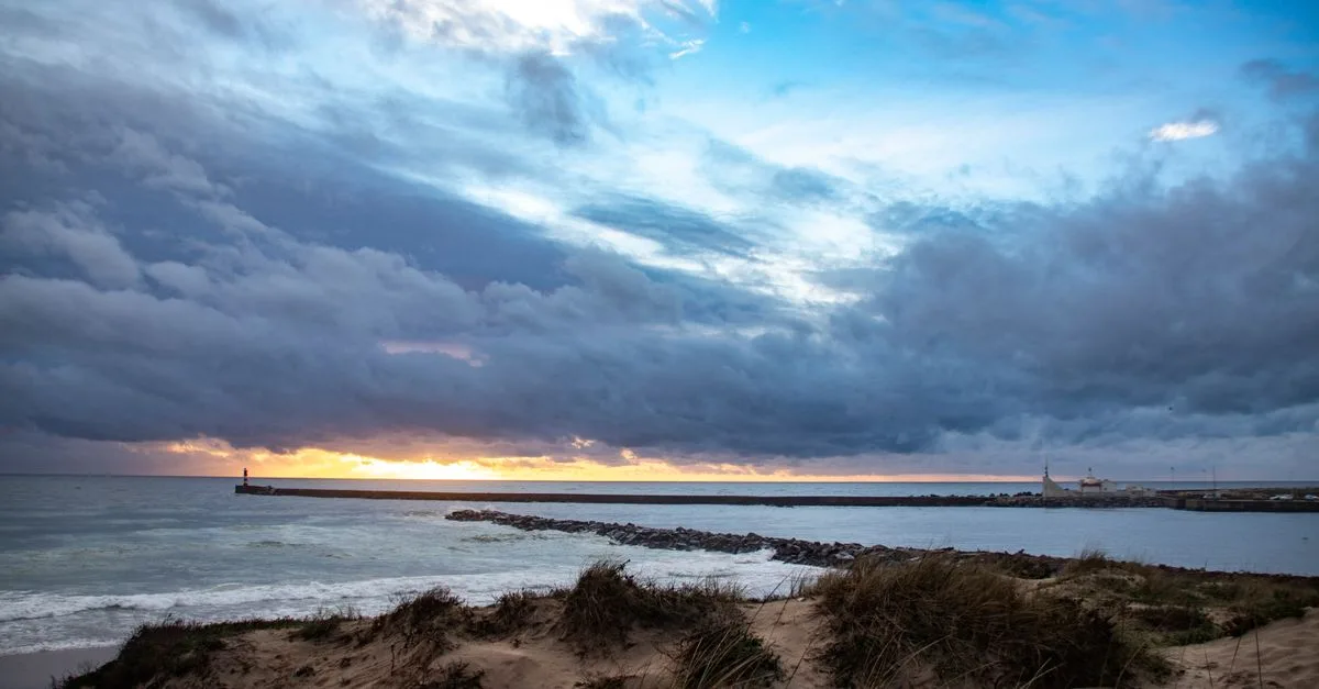 A stunning sunset view over the Praia da Azurara beach in Portugal with dramatic clouds and breakwaters.