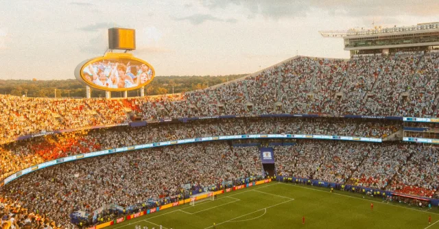 Aerial view of a packed soccer stadium during a lively match at sunset.