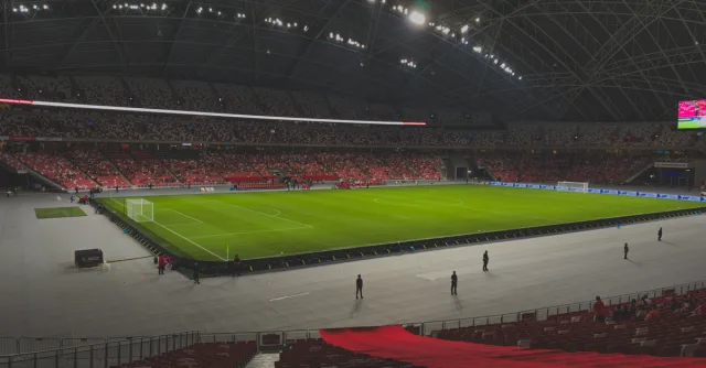 Spacious indoor soccer stadium filled with spectators. Bright lighting enhances the green field.