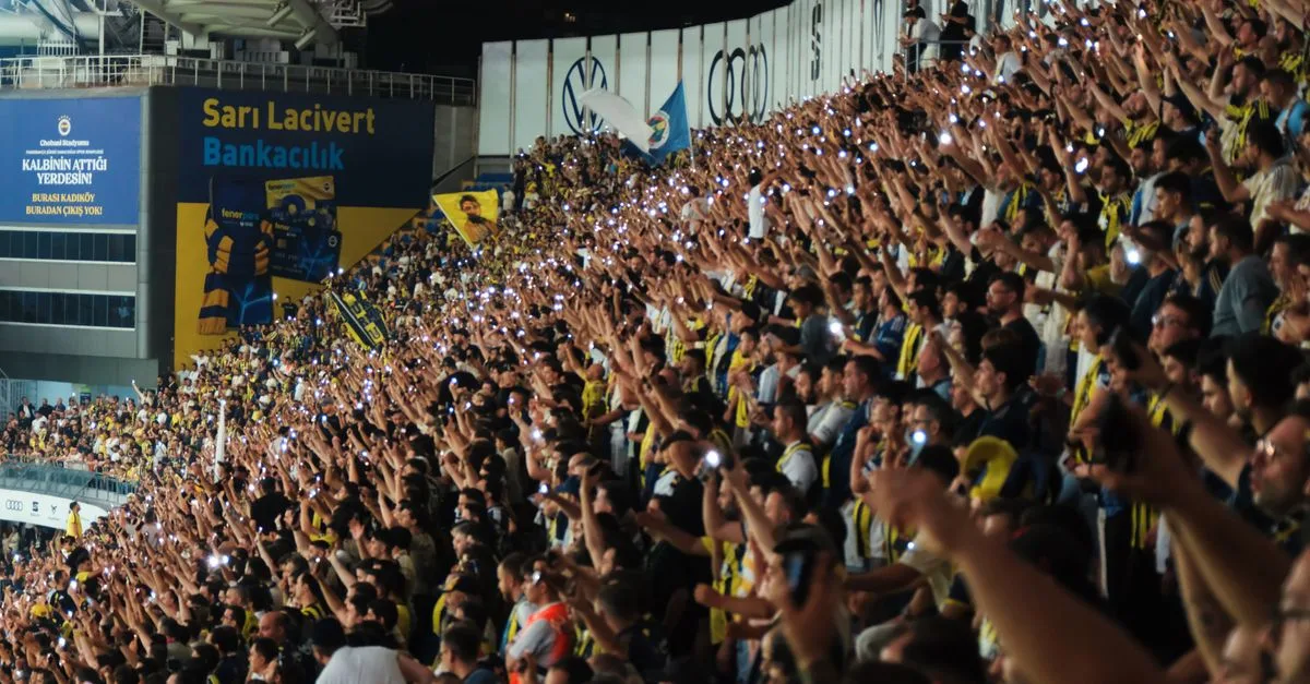 A lively crowd at a football stadium at night, showing unity and excitement with mobile flashlights.