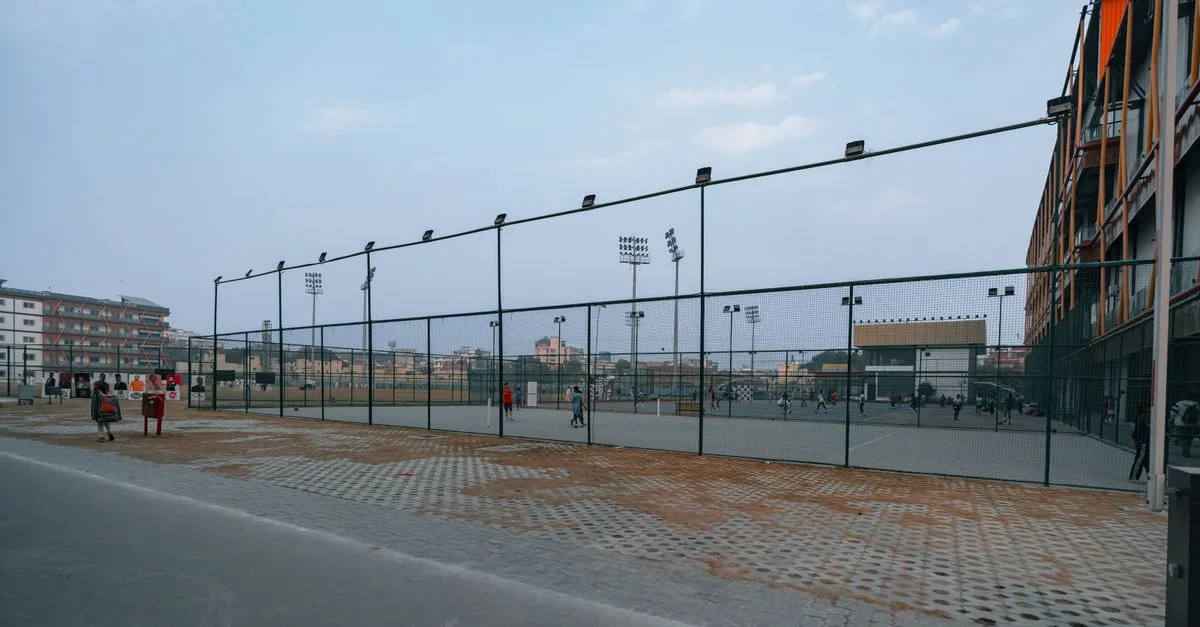 Wide view of a sports complex in Delhi, India, showcasing tennis courts and floodlights under a clear sky.