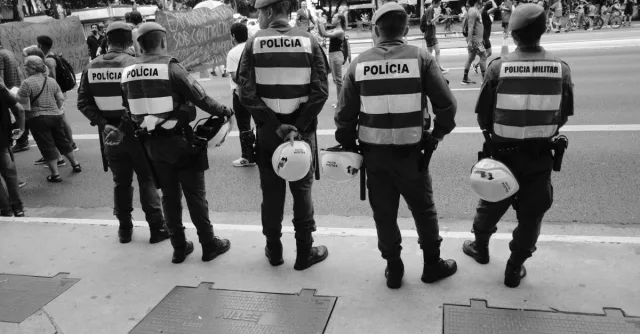 Police officers in uniform observe a street protest during daylight, ensuring safety.