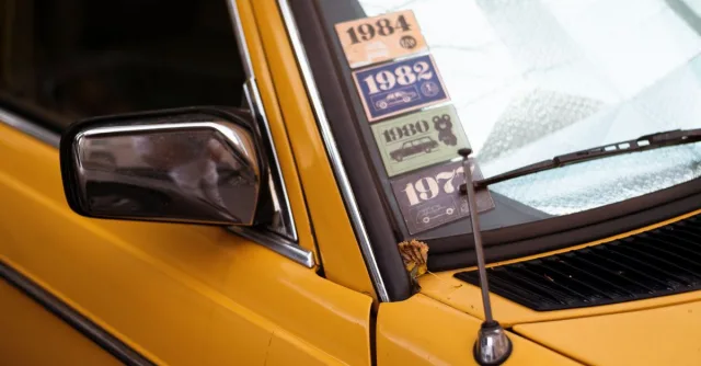 Close-up of a classic yellow car with retro decade stickers on the windshield.