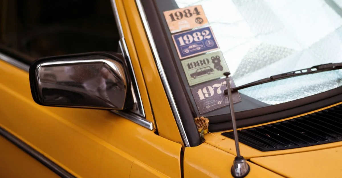 Close-up of a classic yellow car with retro decade stickers on the windshield.