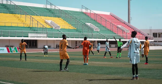 Energetic football match with players in orange and white, vibrant stadium backdrop.
