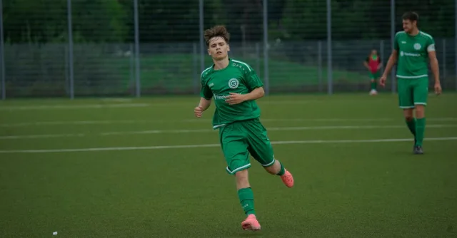 A football player in a green jersey running during an outdoor match on a grass pitch.