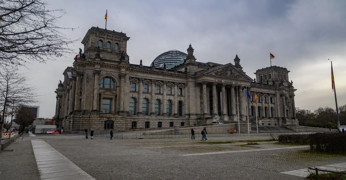 View of the iconic Reichstag building in Berlin under a cloudy sky, featuring its distinctive glass dome.