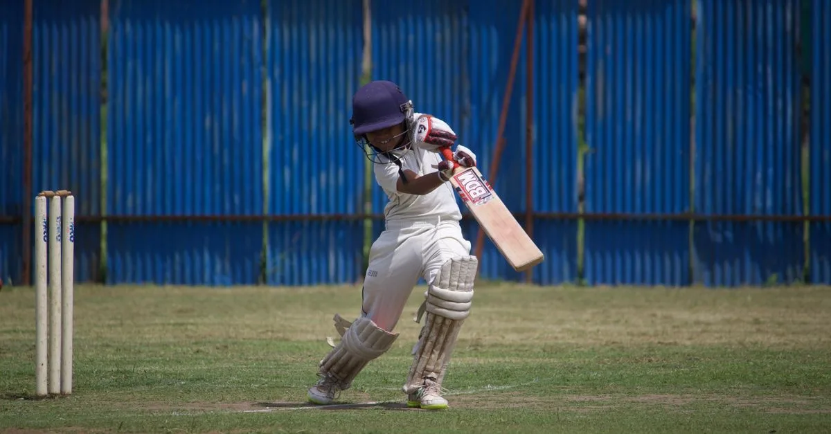A young cricketer in action on a sunny day, playing on a grass field with a bat and wicket.